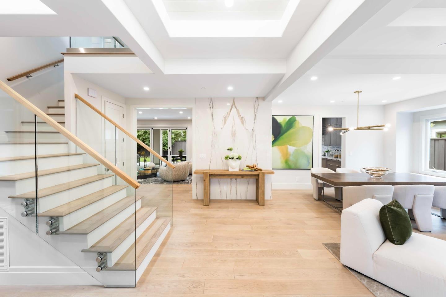Skylit entry with an oak stair, glass balustrade, pale oak floor, and views into the dining and family rooms.